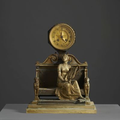 statue en bronze représentant une femme assise sur un banc, avec une horloge au-dessus de sa tête