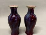 une paire de vases violets posés sur une surface blanche, sur fond blanc