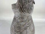 a gray vase with a bird on it sitting on a white surface