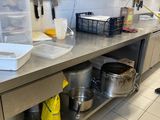 un plan de travail en acier inoxydable sur lequel sont posés des casseroles et des poêles, dans une cuisine professionnelle
