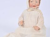 an antique porcelain doll of a baby in a white dress and bonnet