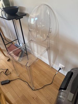 une chaise transparente posée sur un plancher en bois, à côté d'une table