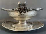 an antique silver plate with a bowl on it on a gray surface
