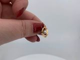 a woman ' s hand holding a gold ring with a pearl on it