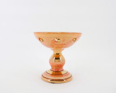 un petit bol en verre orange posé sur un socle doré