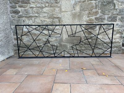 une clôture en fer noir posée sur un sol en briques, avec un mur de pierre en arrière-plan
