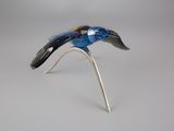 oiseau en verre argenté et bleu perché sur une branche, sur fond gris