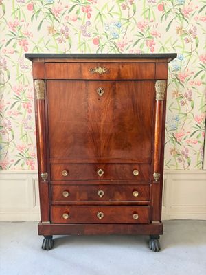 une photo représentant une commode en bois à tiroirs montée sur roulettes, placée devant un mur recouvert de papier peint
