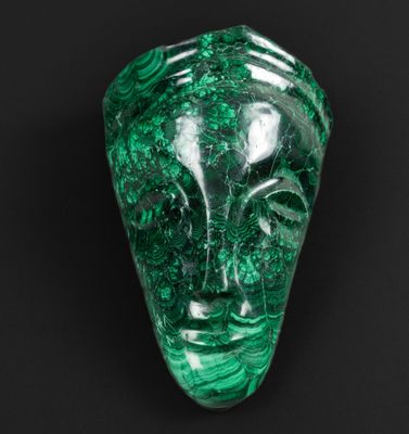 un gros plan d'un masque en pierre verte sur une surface noire