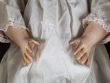 a close up of a doll ' s hands on a white dress