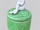une petite boîte verte sur laquelle est posée une figurine représentant une femme assise
