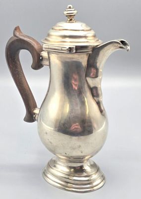 an antique silver coffee pot with a wooden handle sitting on a table