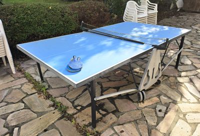 une table de ping-pong bleue sur une terrasse en pierre