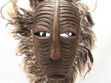 un masque en bois orné de plumes, posé sur un socle