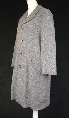 un manteau gris posé sur un mannequin, sur fond noir