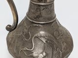 an old silver pitcher with a bird on it sitting on a table