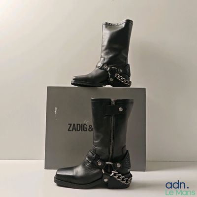 une paire de bottes en cuir noir ornées de chaînes, posée sur une boîte