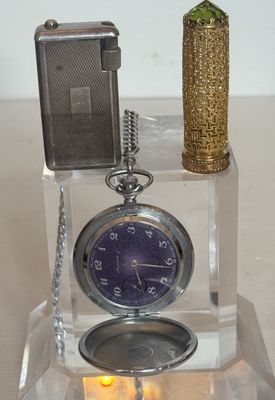 une horloge et un briquet posés sur une table où se trouve une bougie
