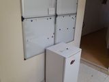 a refrigerator in the corner of a room with a whiteboard on the wall