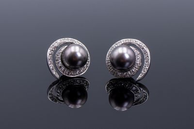 une paire de boucles d'oreilles en perles noires et diamants posées sur une surface réfléchissante