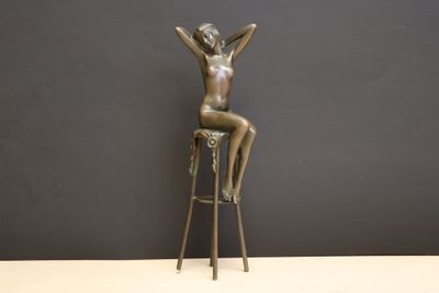 bronze statue of a woman sitting on a stool with her hands up