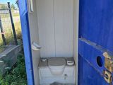 a toilet in a blue portable toilet stall in the grass