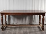 une vieille table en bois posée sur un parquet, à côté d'un rideau blanc