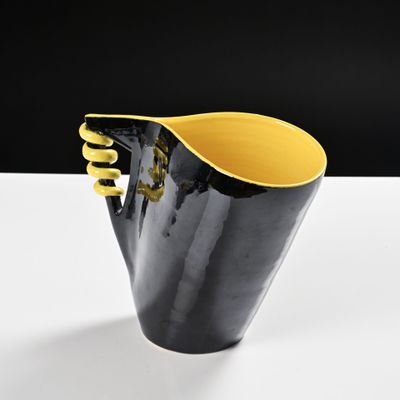 yellow and black vase on a white table with a black background