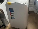 a white air conditioner sitting on the floor next to a desk