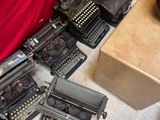 many type of typewriters on the floor next to a bed