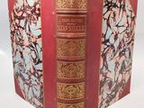 an old book with a red cover and gold trim on it