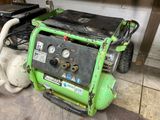 a green air compressor sitting on the floor next to a white teddy bear