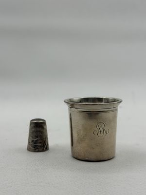 an antique silver thimble next to a silver thimble on a white surface