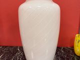 a white vase sitting on a marble table with a red wall behind it