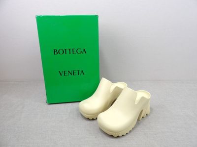 une paire de sabots blancs posée à côté d'une boîte verte de Bottega Veneta