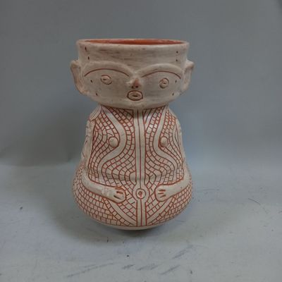 un petit vase orné d'un visage, posé sur une table