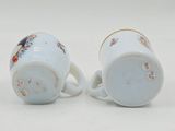 pair of porcelain cups with floral designs on them sitting on a white surface