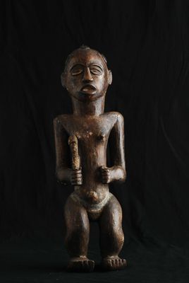 une statue en bois représentant un homme tenant un bébé dans ses bras, sur fond noir