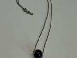 collier composé d'une perle noire montée sur une chaîne en argent, sur un fond blanc