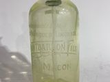 an old green glass bottle with a black cap on a white surface
