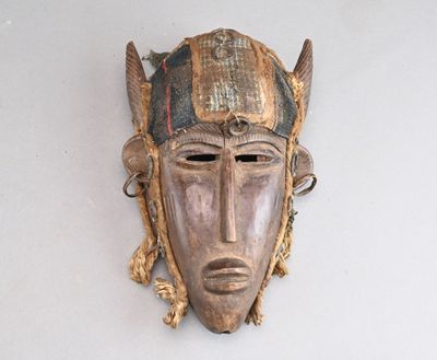 un vieux masque en bois accroché à un mur, orné de plumes