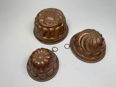 three antique copper molds on a white surface