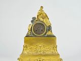 a gold clock with a woman sitting on top of it