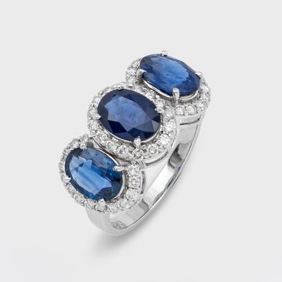 un gros plan d'une bague à trois pierres, sertie de saphirs bleus et de diamants