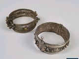 une paire de bracelets en argent posés sur une surface blanche avec un fond bleu