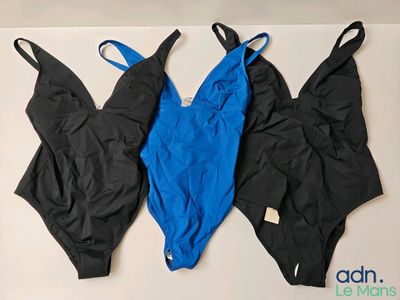 trois maillots de bain noirs et bleus accrochés à un mur blanc