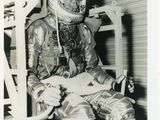 photographie en noir et blanc d'un homme en combinaison spatiale, assis sur une chaise