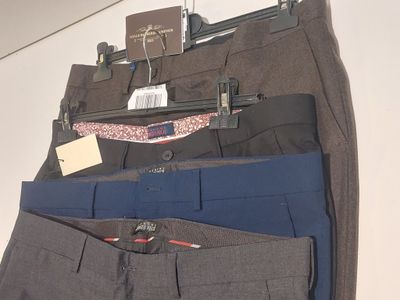 trois pantalons pour homme suspendus à un cintre accroché au mur