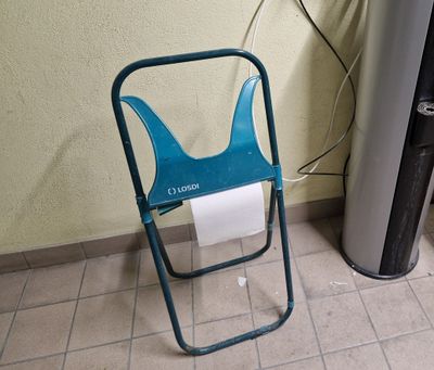 une chaise pliante bleue sur laquelle est posé un rouleau de papier toilette