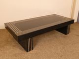une table basse noire avec un plateau en verre, posée sur un sol recouvert de moquette